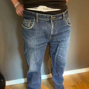  blå jeans straight fit - Säljer blå tvätt med snygga slitningar. Modellen har rak passform, fem fickor och normal midja. Jeansen är tillverkade i robust denim och har tydliga kontrastsömmar. Perfekt för dig som gillar en avslappnad stil.
