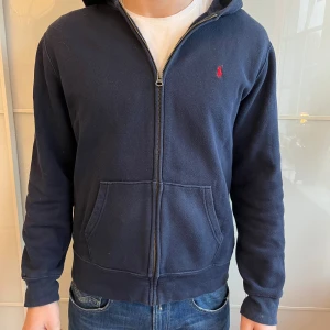 Mörkblå hoodie från Ralph Lauren - Säljer en mörkblå hoodie från Ralph Lauren med dragkedja och huva. 