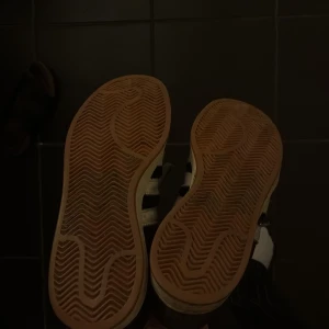 Adidas Campus sneakers svart/vit - Säljer ett par klassiska Adidas Campus sneakers i svart mocka med vita ränder och vit sula. Skorna har snörning och den ikoniska Campus-loggan på sidan. Perfekta för dig som gillar retrostil och streetwear.