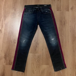 Sjukt unika Replay jeans med röd sidoremsa 28/28 - Snygga mörkblå Replay jeans med slitningar och råa benslut. De har en röd och brun sidoremsa i sammet längs benen som ger en cool kontrast. Klassisk femficksmodell med dragkedja och knapp. Perfekt för dig som vill sticka ut lite extra. Midja 39cm längd 98cm (70)