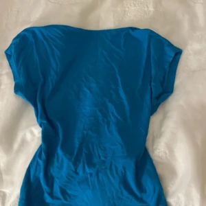 Blå topp med öppen rygg - Säljer en blå topp med öppen rygg och korta ärmar. Toppen har en tight passform och är tillverkad i mjukt bomullsmaterial. Perfekt för dig som gillar en enkel men snygg look med lite edge. Framhäver ryggen fint.🩵