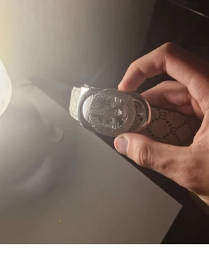 Bälte med glittrigt spänne - Säljer ett bälte med ett stort, glittrigt spänne i silverfärg och mönstrat band. Perfekt accessoar för att lyfta din outfit med lite extra bling.