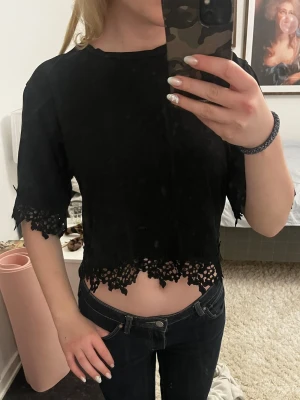 Svart t-shirt med spetsdetaljer - Säljer en svart T-shirt från Zara med snygga spetsdetaljer vid ärmslut och nederkant. Den har korta ärmar och en rund halsringning. Perfekt för dig som gillar en stilren look med lite extra edge.
