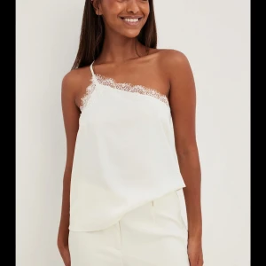 Oneshouldertopp NA-KD - Festlig vit oneshouldertopp med spetsdetaljer! Från NA-KD i ett satinliknande material. Storlek 36/S. Enbart använd en gång! 98% Polyester, 2% Elastan.