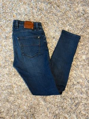 Mörkblå jeans från Tramarossa - Säljer ett par mörkblå jeans från Tramarossa med snygga röda sömmar och detaljer. Modellen har klassisk femficksdesign, knappgylf och en skön passform som sitter snyggt på benen. Materialet är mjukt jeans-tyg med coola broderier på insidan.
