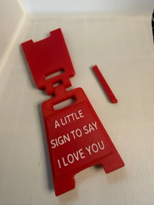 Röd miniskylt med kärleksbudskap - Säljer en liten röd skylt i plast med vit text: 'A little sign to say I love you'. Skylten är vikbar och har en klassisk A-formad design, perfekt som gullig dekoration eller present till någon du gillar.