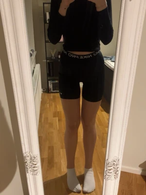 Nike Pro svarta träningsshorts - Nike Pro svarta träningsshorts med hög midja och elastisk linning med logga. Tight passform och tillverkade i stretchigt syntetmaterial som andas. Perfekta för gymmet eller löpning. Snygg och sportig look med diskret Nike-logga på benet.