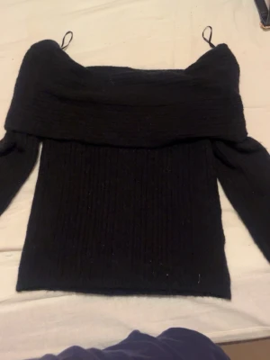 Svart offshoulder stickad tröja - Säljer en svart stickad tröja med offshoulder-design och ribbad struktur. Tröjan har långa ärmar och bred krage som vilar över axlarna. Perfekt för dig som vill ha en stilren och trendig look med lite extra edge. Etikett tyvärr borta men skulle gissa att den är från H&M och storlek Xxs-Xs 💓