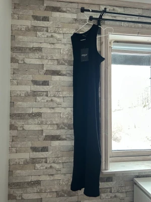 Svart ribbad långklänning från ONLY - Säljer en svart långklänning från ONLY med ribbad struktur. Klänningen är ärmlös och har en enkel, rak passform som ger en clean look. Perfekt att styla med sneakers eller boots för en trendig vibe.