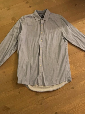Blåmönstrad skjorta Tommy Hilfiger - Säljer en slim fit skjorta från Tommy Hilfiger i storlek L.  Skjortan är blå och vit med ett småprickigt mönster, klassisk krage och knappar framtill. Materialet är mjuk bomull och den har det ikoniska Hilfiger-logotypen broderad på bröstet. Nypris 1300:-