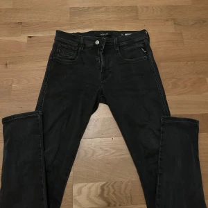 Svarta Replay jeans, midja 30/32 - Svarta jeans från Replay med klassisk femficksdesign och dragkedja. Modellen har smal passform och raka ben. Snygga detaljer på bakfickorna och diskret Replay-logga vid fickan. Perfekta för dig som gillar stilrena och bekväma jeans. Ett litet hål mellan bena som man kan se i bild fyra.