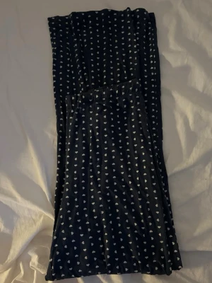 Mörkblå byxor med hjärtmönster 157 - Mörkblå mjuka byxor från 157 med vita hjärtan över hela tyget. Byxorna har resår i midjan och är tillverkade i ett stretchigt och bekvämt material, perfekta för chill dagar hemma. Snyggt och lekfullt mönster som sticker ut.