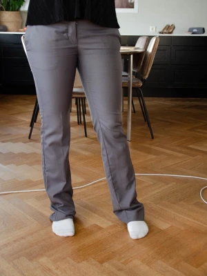 Grå kostymbyxor från Vero Moda - Säljer ett par stilrena grå kostymbyxor från Vero Moda i storlek 36. Byxorna har raka ben, midwaist passform och stängs med dragkedja och knapp framtill. Snygga detaljer med knappar vid fickorna och skönt material som passar perfekt till en dressad look.