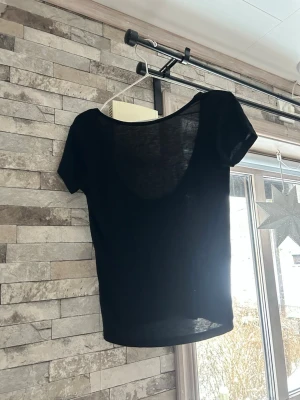 Svart tunn kortärmad topp - Svart, tunn och lätt topp med korta ärmar och djup rundad rygg. Enkel och stilren design, perfekt att matcha med jeans eller kjol. Materialet känns mjukt och luftigt, vilket gör den skön att bära under varmare dagar. Öppen i ryggen 