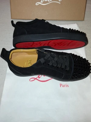 Christian Louboutin - Hej! Säljer mina Christian Louboutin med röda sulor och svarta nitar på tån. Skorna är i mocka med rund tå och har breda svarta skosnören. Priset kan diskuteras.