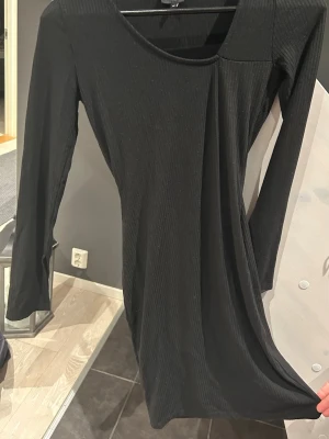 Svart ribbad långärmad klänning - Säljer en svart klänning med ribbad struktur och lång ärm. Klänningen har en rund halsringning och är i en mjuk, stretchig kvalitet som sitter snyggt på kroppen. Perfekt för dig som gillar enkel och stilren design.