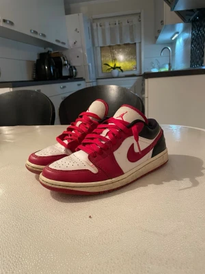 Nike Air Jordan 1 Low röd/vit - Säljer ett par Nike Air Jordan 1 Low med klassisk röd, vit och svart färgkombination. Skorna har röd swoosh, röda snören och perforerad tåbox. Ovandelen är i skinn och sulan är vit med röd yttersula. Perfekta för dig som gillar streetwear och sneakers.