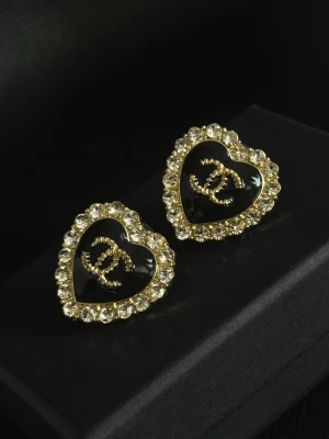 Örhängen - Ett par hjärtformade örhängen med svart och guld samt glittrande stenar runt kanten.