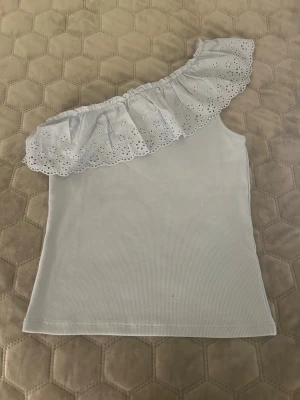 Ljusblå oneshoulder topp Kappahl - Säljer en ljusblå ribbad oneshoulder topp från Kappahl i storlek 170. Toppen har en bred volang med broderade hål och blommönster längst axeln💕nyskick men har ej prislapp kvar!