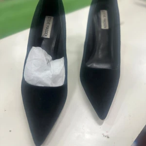 Svarta pumps från Steve Madden - Säljer ett par klassiska svarta pumps från Steve Madden i mocka. Skorna har spetsig tå och hög klack, vilket ger en elegant och tidlös look. Insidan är fodrad med syntet och yttersulan är i gummi. Perfekta för dig som vill ha en stilren och chic sko.