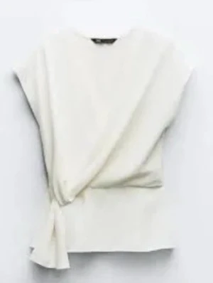 Vit omlottopp med knyt - Snygg vit topp med omlottdesign och knyt i sidan. Toppen är ärmlös och har en stilren, minimalistisk look som passar perfekt till jeans eller kjol. Materialet känns mjukt och lätt, vilket gör den skön att bära under varmare dagar.