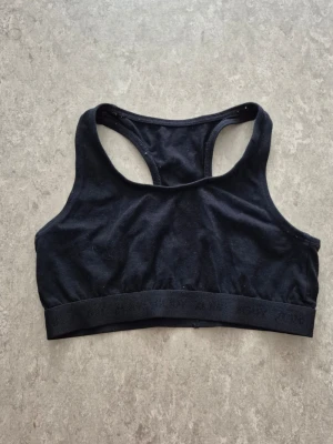 Sport-behå - En enkel och stilren svart sport-behå från KappAhl i stretchigt bomullsmaterial. Sport-behå har brottarrygg och bred resår nedtill med diskret text. Perfekt för träning eller som basplagg.