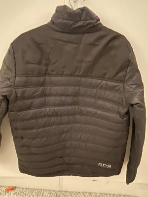 Svart pufferjacka från Bluewear Pro - Säljer en svart pufferjacka från Bluewear Pro Workwear i storlek M. Jackan har quiltad design, hög krage och flera dragkedjeförsedda fickor. Perfekt för kyliga dagar och har en clean look med diskret logga på bröstet och axeln.