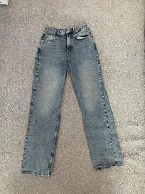 Blåa raka jeans från NA-KD - Säljer ett par blåa raka jeans från NA-KD med hög midja. Jeansen har en tvättad look och raka ben, perfekt för en chill och stilren vibe. Materialet är jeans och de har bälteshällor samt knapp- och dragkedjestängning.