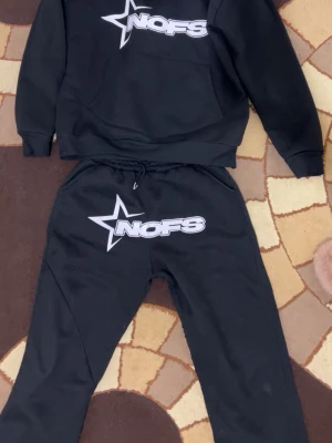 Svarta mjukisbyxor NOFS stl S - Svarta mjukisbyxor från NOFS i storlek S. Byxorna har resår och snörning i midjan samt en stor vit stjärna och NOFS-logga tryckt framtill. Sköna och perfekta för chill eller träning.