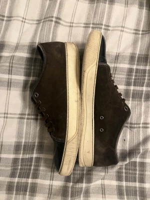 Bruna sneakers från Lanvin med lackad tå - Säljer ett par bruna sneakers från Lanvin med snygg kontrast mellan mocka och svart lackad tå. Skorna har vita gummisulor, bruna skosnören och metallöljetter. Perfekta för dig som gillar stilrena men ändå unika sneakers.                                                   PRISET KAN SJÄLVKLART DISKUTERAS!!