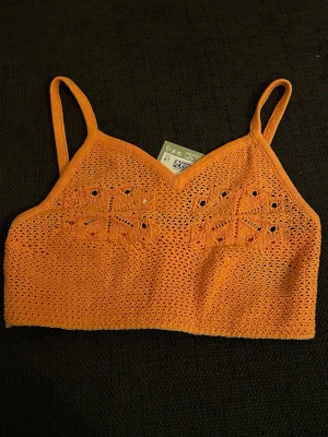 Orange virkad linnetopp från H&M - Säljer en orange virkad linnetopp från H&M i storlek S. Toppen har tunna axelband och ett snyggt hålmönster framtill. Perfekt för sommardagar och festivaler. Materialet är mjukt och luftigt, vilket gör den superbekväm att bära. Helt ny med prislappen kvar 