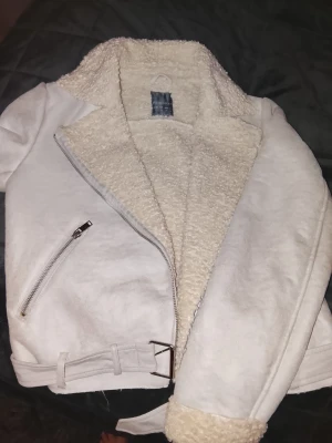 Vit teddyjacka från Primark - Säljer en supermjuk och fluffig vit teddyjacka från Primark. Jackan har stora slag, dragkedja i silver, ficka med dragkedja och bälte nedtill. Insidan är fodrad med mysig teddy och ärmarna har uppvikta muddar. Perfekt för dig som vill ha en cozy och trendig look.