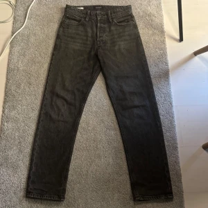 Svarta loose fit jeans Jack & Jones - Säljer ett par svarta jeans från Jack & Jones, modell Loose/Chris. Jeansen har loose fit, raka ben. Materialet är jeans och färgen är tvättad svart. Jeansen är lite slitna nertill och det kan man se på sista bilden. Förutom de  är jeansen i bra skick och Perfekta för en avslappnad och trendig look. Storlek: 28 30