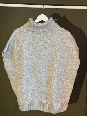 Ljusgrå stickad väst med polokrage - Säljer en ljusgrå stickad väst med hög polokrage och ribbade kanter. Västen är ärmlös och har en avslappnad passform, perfekt att bära över en skjorta eller långärmad tröja. Materialet känns mjukt och mysigt. Köpt från SHEIN, använts en gång🩶