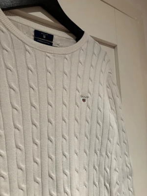 Vit kabelstickad tröja från Gant - Kabelstickad vit tröja från Gant i mjukt stretch bomull. Tröjan är i näst intill nyskick! Inga defekter , hål eller fläckar!