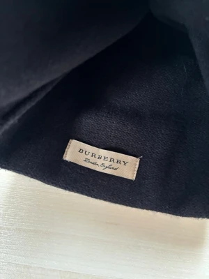 Svart mössa med logga - Snygg svart mössa från …… med bred vit logotyp runt kanten. Klassisk beanie-modell i mjukt stickat material, perfekt för att hålla värmen och ge en stilren look. Passar dig som vill ha en exklusiv accessoar med tydlig branding.