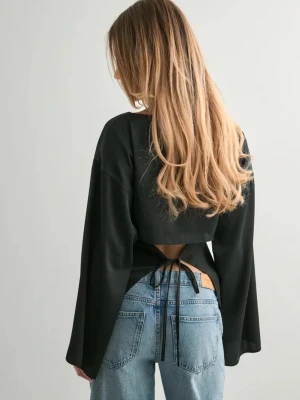 Satintopp med öppen rygg från Nelly - Säljer en svart blus i satin med vida ärmar och öppen rygg som knyts med tunna band baktill. Toppen har en slät, lätt glansig yta. Storlek 34, prislappen kvar då den aldrig kommer till användning 