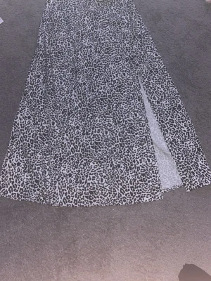Lång leopardmönstrad kjol med slits - Snygg långkjol med svartvitt leopardmönster och en cool slits på sidan. Perfekt för dig som vill sticka ut med en trendig look. Kjolen har en rak passform och är lätt och flowy i materialet.