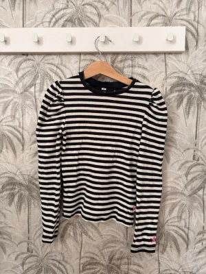 Randig långärmad topp från WE - Säljer en svartvit randig långärmad topp från WE med puffiga axlar och rund hals. Den har en liten fläck på högre bakre ärmen men får nog bort i tvätten. Toppen är ribbad och har en liten rosa detalj vid ärmslutet. Perfekt för dig som gillar en enkel men trendig stil.