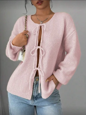 Ljusrosa stickad cardigan med rosetter - Supersöt ljusrosa stickad cardigan med tre knytrosetter framtill. Tröjan har en avslappnad passform, långa ärmar och ribbade muddar. Perfekt att slänga över ett linne eller t-shirt för en chill look.