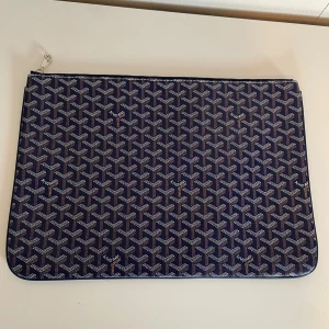 Blå snygg dataväska  - Snygg blå dataväska med ikoniskt grafiskt mönster i vitt och grått. Väskan har dragkedja upptill och insida i beige med präglad logotyp. Perfekt för laptop eller dokument, och ger en lyxig touch till din look.