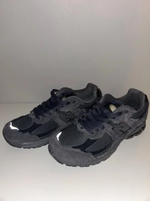 Mörkgrå New Balance sneakers - Snygga mörkgrå New Balance sneakers med mesh och mocka-paneler. Skorna har klassisk snörning, reflekterande detaljer och rund tå. Perfekta för dig som gillar stilrena och sportiga sneakers med en modern vibe.