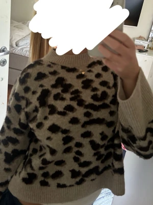 Beige leopardmönstrad stickad tröja - Stickad tröja i beige med svart leopardmönster. Tröjan har en rak passform, ribbad rund halsringning samt ribbade muddar vid ärmslut och nederkant. Perfekt för dig som gillar djurmönstrat och vill ha en trendig look.