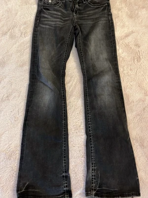 Svarta bootcut jeans med slitningar - Snygga svarta bootcut jeans med slitna detaljer och kontrastsömmar. Jeansen har klassisk femficksdesign och en lätt tvättad look som ger en cool vibe. Perfekta för dig som gillar en avslappnad men trendig stil.