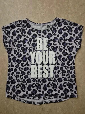 T-shirt - Snygg kortärmad t-shirt från mywear Active med leopardmönster i svart och blått på ljus bakgrund. Stor vit text 'BE YOUR BEST' framtill. Perfekt för dig som vill sticka ut med ett coolt statement-plagg.