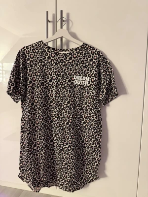 Leopardmönstrad nattlinne - Leopardmönstrad pyjamas med texten 'DREAM OUTFIT' på bröstet. Nattlinnet har korta ärmar och rund hals. Färgerna är beige, svart och ljusrosa. Perfekt för chilliga kvällar eller mysiga morgnar.