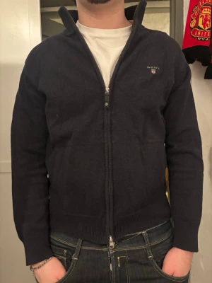 Mörkblå ziptröja från Gant - Säljer en mörkblå ziptröja från Gant med hög krage och diskret logga på bröstet. Tröjan har ribbade muddar och nederkant samt hel dragkedja framtill. Perfekt för lager-på-lager och enkel att matcha med jeans. Ursprungspris 1000