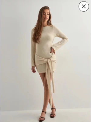 Beige omlottklänning med knyt - Trendig beige kortklänning med lång ärm och snyggt knyt i midjan. Klänningen är endast använd 1 gång💕