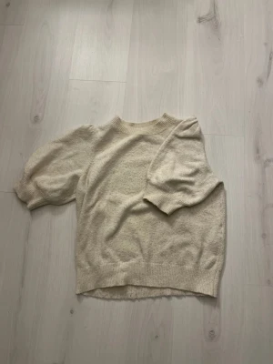 Krämvit stickad tröja Vero Moda - Krämvit stickad tröja från Vero Moda med puffiga, halvlånga ärmar. Tröjan har en rund halsringning och är gjord i ett mjukt material som känns skönt mot huden. Lite nopprig efter tvättar 