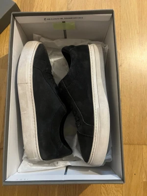 Svarta mockasneakers med vit sula - Stilrena svarta sneakers i mocka med tjock vit platt sula och snörning. Perfekta för dig som gillar minimalistisk design och vill ha ett par klassiska skor till vardagslooken. Skorna har rund tå och diskreta detaljer. Box kommer också med.
